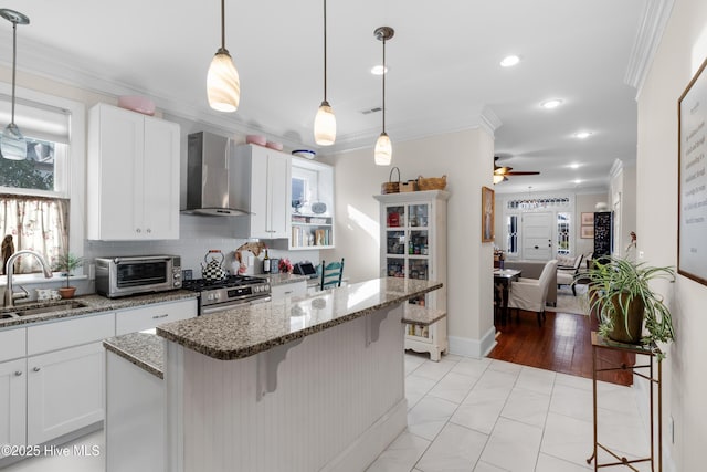 kitchen with a breakfast bar, stainless steel range with gas stovetop, a sink, crown molding, and wall chimney exhaust hood