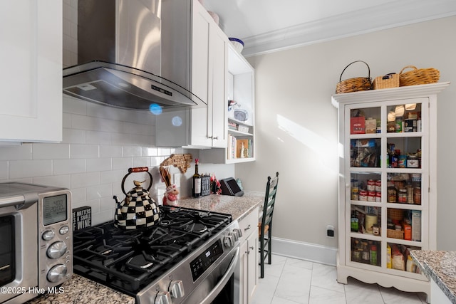 kitchen with stainless steel gas range oven, ornamental molding, backsplash, white cabinetry, and wall chimney range hood