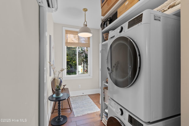 washroom with stacked washer / dryer, laundry area, baseboards, and wood finished floors