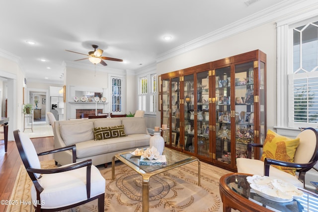 living area with ornamental molding, wood finished floors, visible vents, and ceiling fan