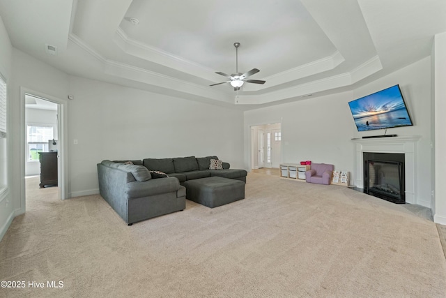 living area with carpet flooring, a raised ceiling, a fireplace with flush hearth, and ornamental molding