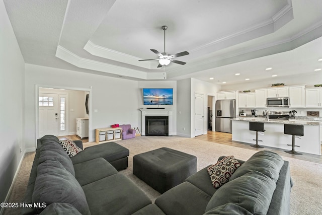 living room with a glass covered fireplace, light colored carpet, crown molding, and a raised ceiling