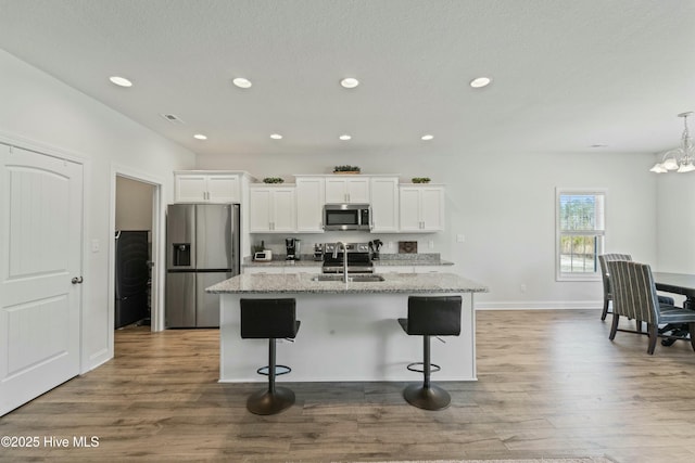 kitchen with a breakfast bar, a kitchen island with sink, a sink, stainless steel appliances, and white cabinets