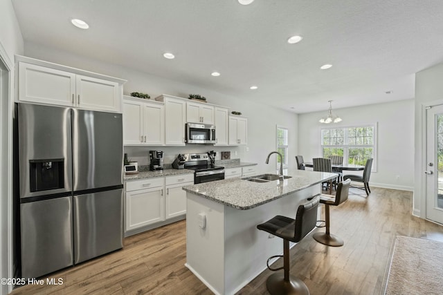 kitchen with a breakfast bar, a sink, white cabinets, light wood-style floors, and appliances with stainless steel finishes