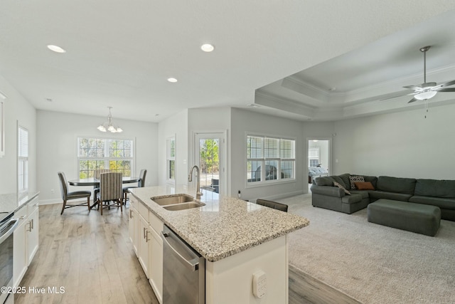 kitchen with a center island with sink, light wood-style flooring, a sink, white cabinets, and stainless steel dishwasher