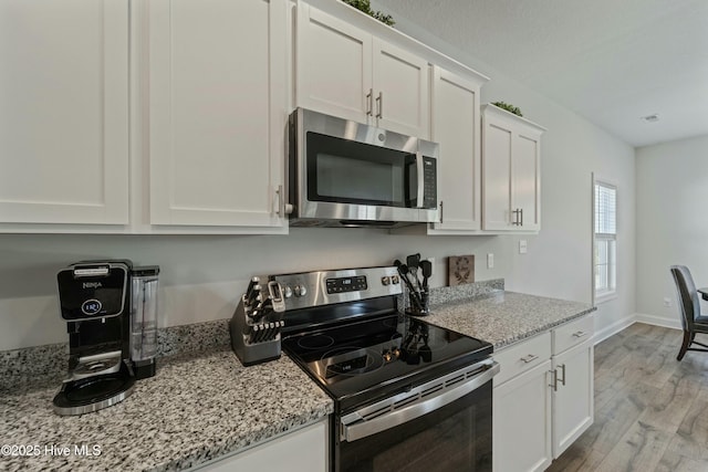 kitchen featuring light wood finished floors, baseboards, light stone countertops, stainless steel appliances, and white cabinetry