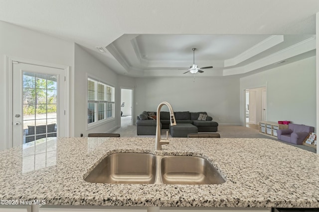 kitchen with a sink, a raised ceiling, open floor plan, and light stone countertops