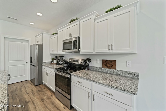 kitchen with visible vents, light stone counters, wood finished floors, white cabinetry, and appliances with stainless steel finishes