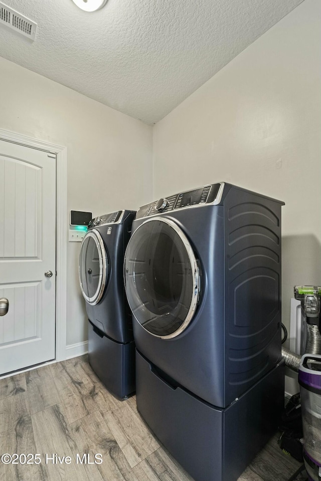 clothes washing area featuring visible vents, light wood-type flooring, laundry area, a textured ceiling, and separate washer and dryer