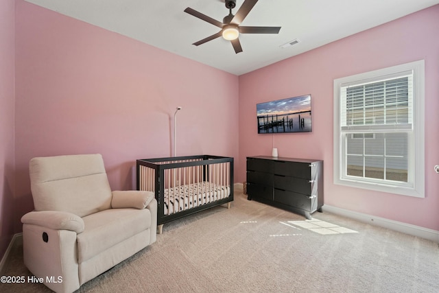 carpeted bedroom featuring visible vents, a nursery area, baseboards, and ceiling fan