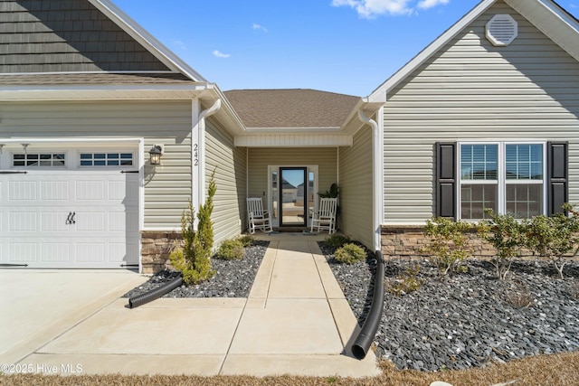 view of exterior entry featuring stone siding, a shingled roof, and a garage