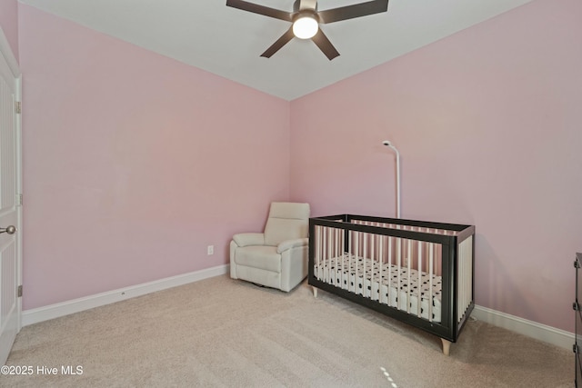 carpeted bedroom featuring a nursery area, baseboards, and ceiling fan