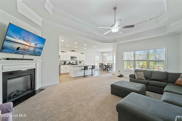 living room featuring baseboards, a tray ceiling, a fireplace with flush hearth, ornamental molding, and light carpet