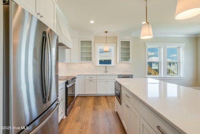kitchen with stainless steel appliances, a sink, white cabinetry, decorative backsplash, and glass insert cabinets