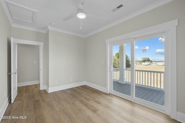 unfurnished room with visible vents, wood finished floors, crown molding, baseboards, and attic access