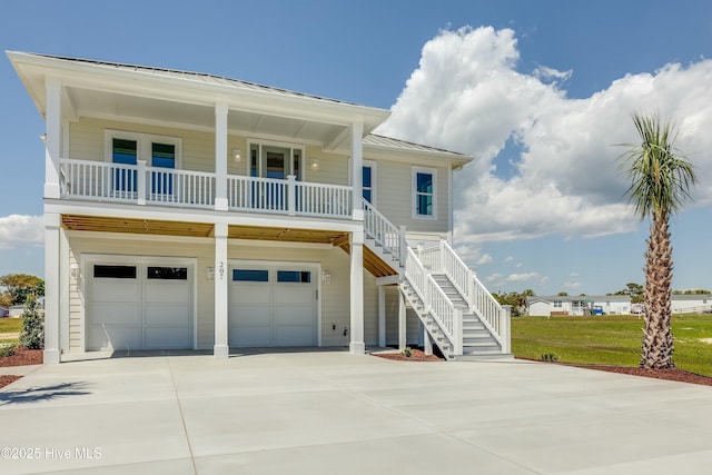raised beach house with concrete driveway, covered porch, an attached garage, metal roof, and a standing seam roof
