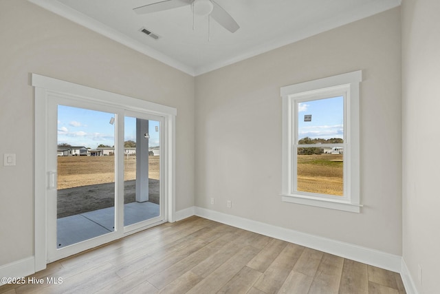 spare room featuring visible vents, ornamental molding, a ceiling fan, wood finished floors, and baseboards