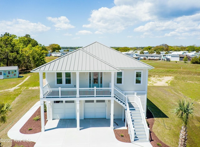 raised beach house with driveway, covered porch, metal roof, a garage, and stairs