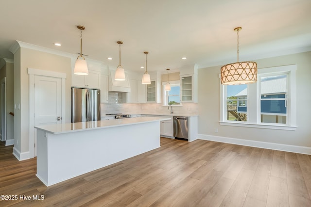 kitchen featuring white cabinets, stainless steel appliances, a center island, backsplash, and light countertops