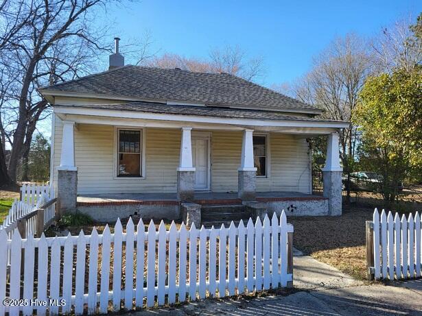 craftsman house with a fenced front yard, covered porch, and a shingled roof