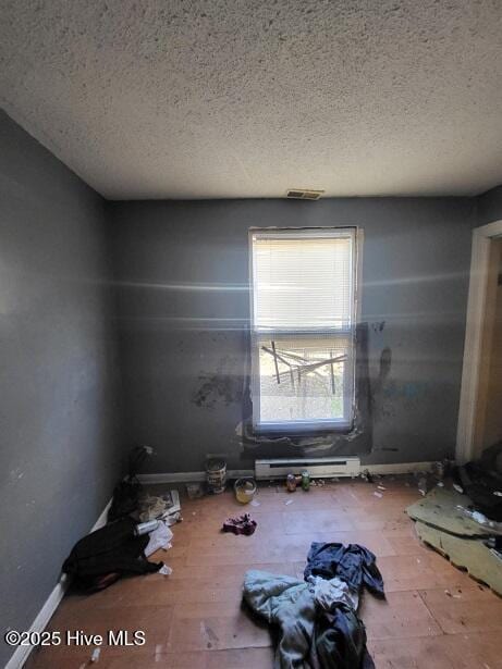 unfurnished room featuring a baseboard heating unit, baseboards, and a textured ceiling