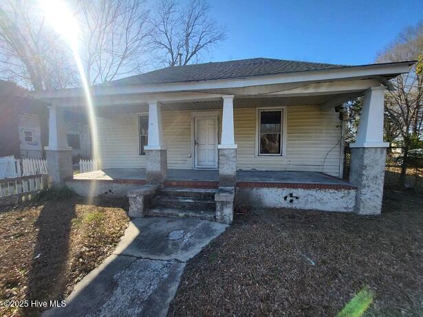 view of front of house with fence, covered porch, and a shingled roof