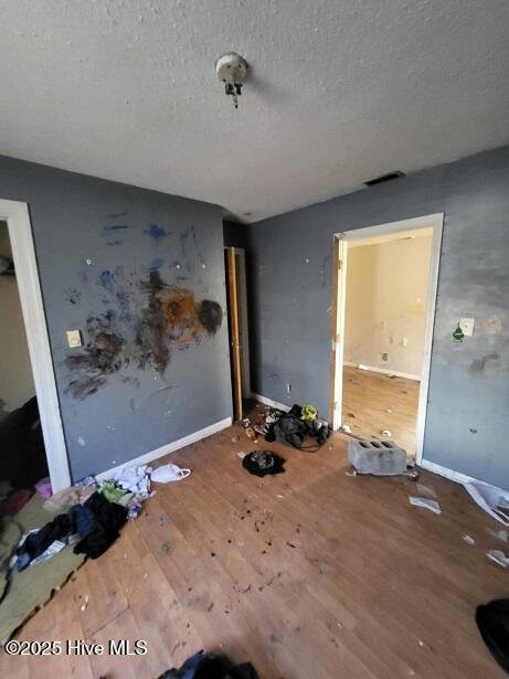 unfurnished bedroom featuring visible vents, wood finished floors, baseboards, and a textured ceiling