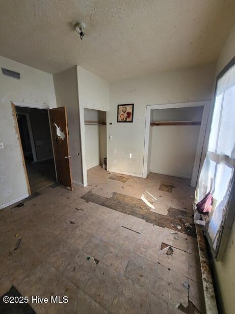 unfurnished bedroom with two closets and a textured ceiling