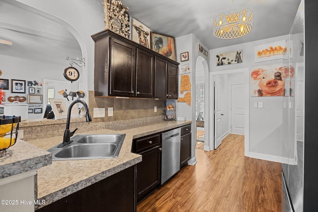 kitchen featuring light wood finished floors, arched walkways, a sink, light countertops, and stainless steel dishwasher