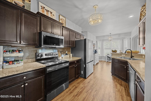 kitchen with tasteful backsplash, light wood-style flooring, appliances with stainless steel finishes, an inviting chandelier, and a sink