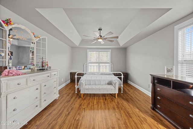 bedroom featuring a tray ceiling, multiple windows, baseboards, and wood finished floors