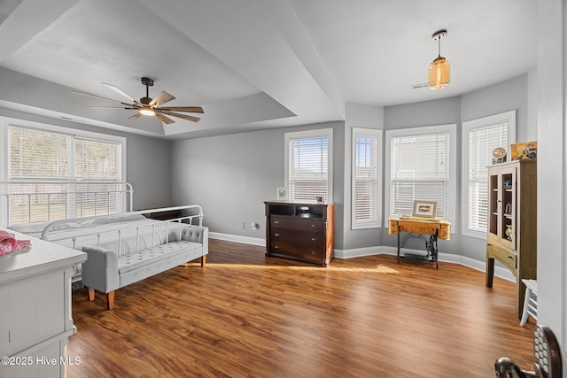 bedroom featuring a tray ceiling, multiple windows, wood finished floors, and baseboards