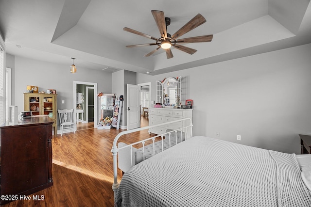 bedroom with a ceiling fan, a raised ceiling, and dark wood-type flooring