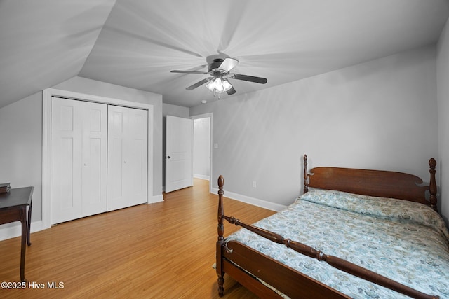 bedroom with light wood-type flooring, lofted ceiling, a closet, baseboards, and ceiling fan