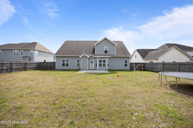 rear view of house with a patio, a trampoline, a fenced backyard, and a yard