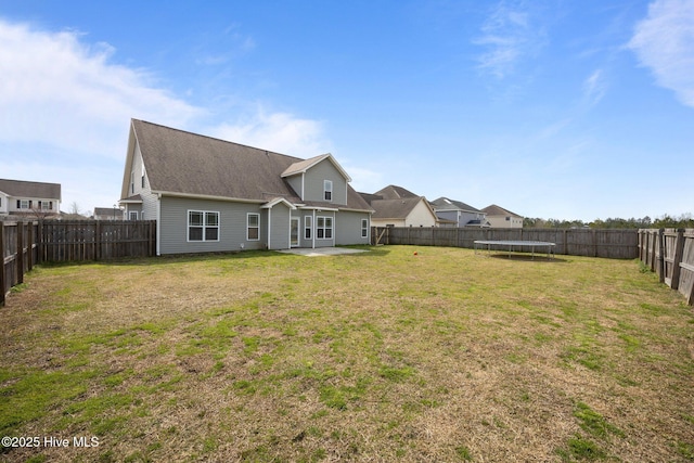 rear view of property with a yard, a fenced backyard, a patio, and a trampoline