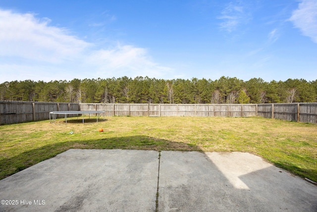 view of yard with a fenced backyard, a patio, a forest view, and a trampoline