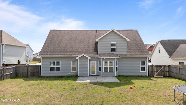 back of house featuring a fenced backyard, a shingled roof, a trampoline, a patio area, and a lawn