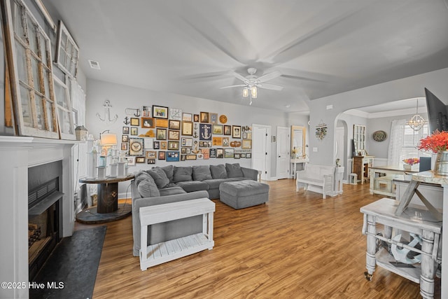 living room featuring wood finished floors, a fireplace with flush hearth, arched walkways, and ceiling fan