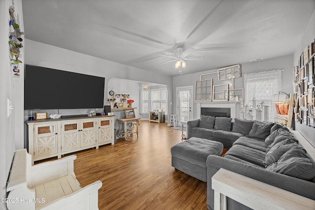 living room with arched walkways, a fireplace, wood finished floors, and a ceiling fan