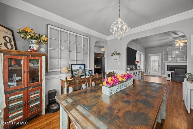 dining room with arched walkways, ceiling fan with notable chandelier, wood finished floors, and ornamental molding