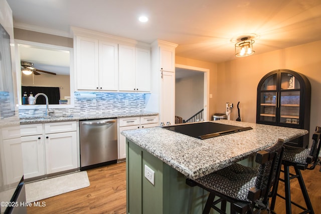 kitchen featuring a kitchen island, a breakfast bar, stainless steel dishwasher, black electric cooktop, and a sink