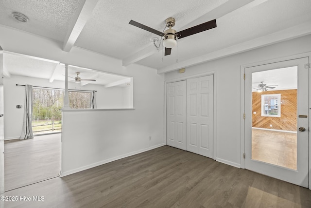 interior space with beam ceiling, wood finished floors, baseboards, and a textured ceiling