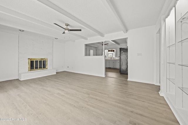 unfurnished living room with a brick fireplace, baseboards, ceiling fan, beamed ceiling, and light wood-style floors