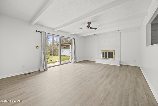 unfurnished living room with beamed ceiling, visible vents, a textured ceiling, wood finished floors, and a brick fireplace