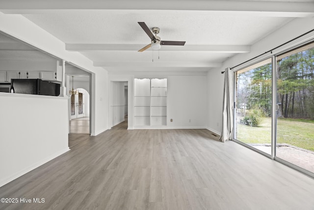 unfurnished living room with beamed ceiling, light wood-style flooring, baseboards, and a textured ceiling