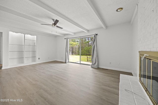 unfurnished living room featuring wood finished floors, baseboards, beam ceiling, a fireplace, and a textured ceiling