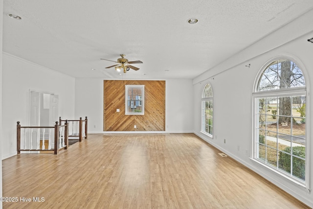 spare room with wooden walls, baseboards, light wood-style flooring, a textured ceiling, and an accent wall