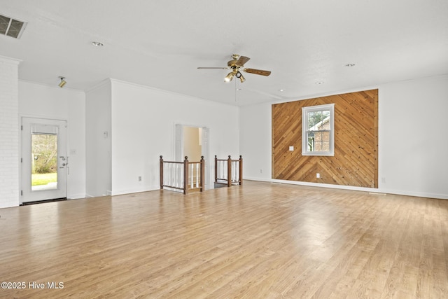 unfurnished room with a wealth of natural light, visible vents, wooden walls, and light wood-style flooring