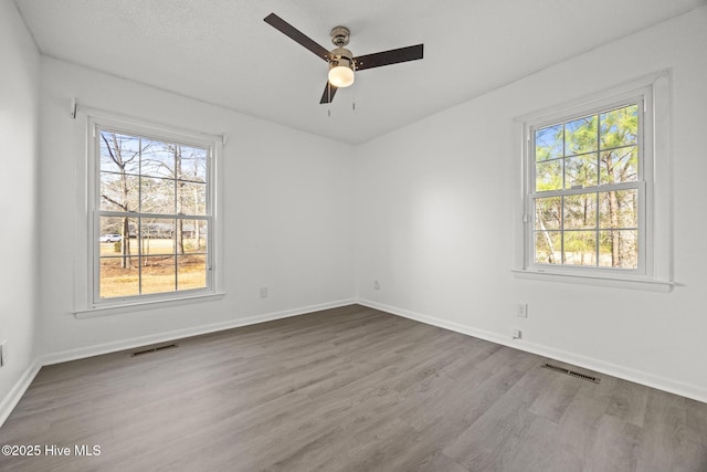 empty room with a ceiling fan, wood finished floors, visible vents, and baseboards